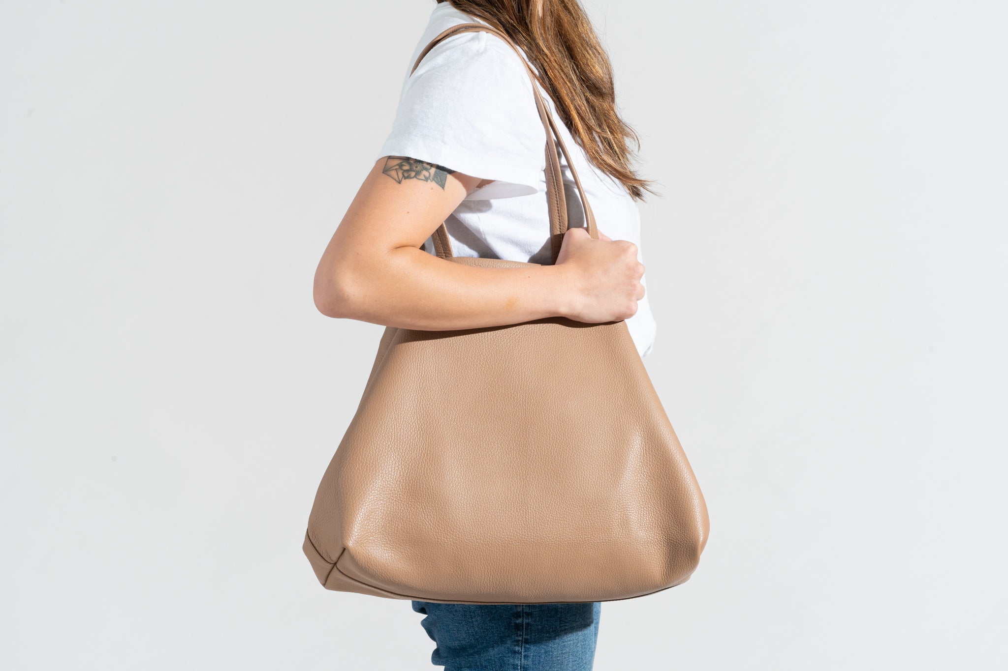 A person wears the Cuyana Classic Easy Tote with its shape bent in at the sides to take up less space.