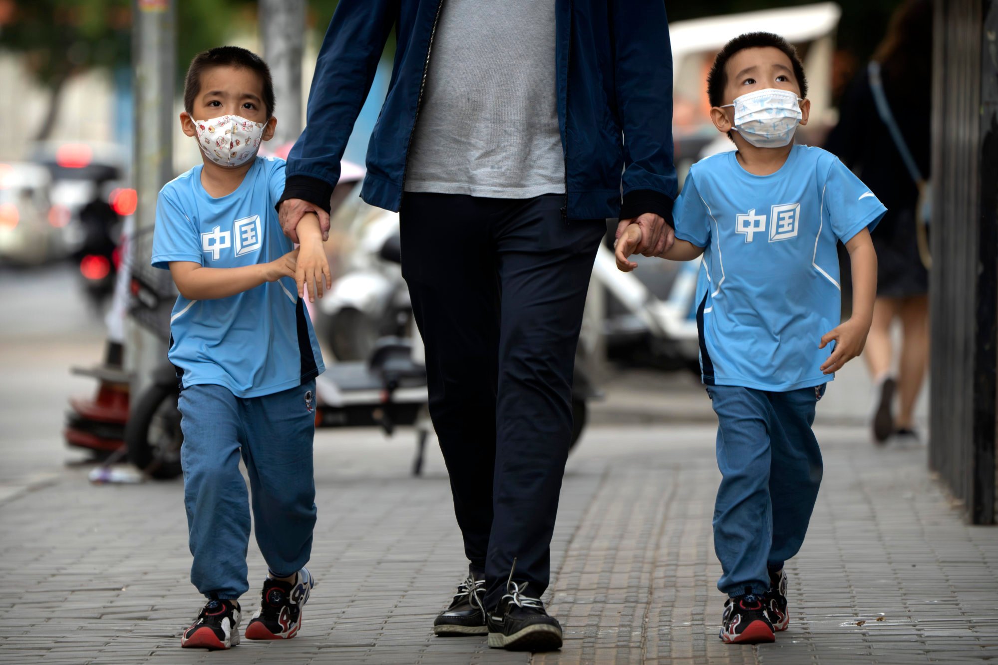 Boys wearing face masks and t-shirts that say ‘China’ walk along a street in Beijing, May 18, 2023. Photo: AP