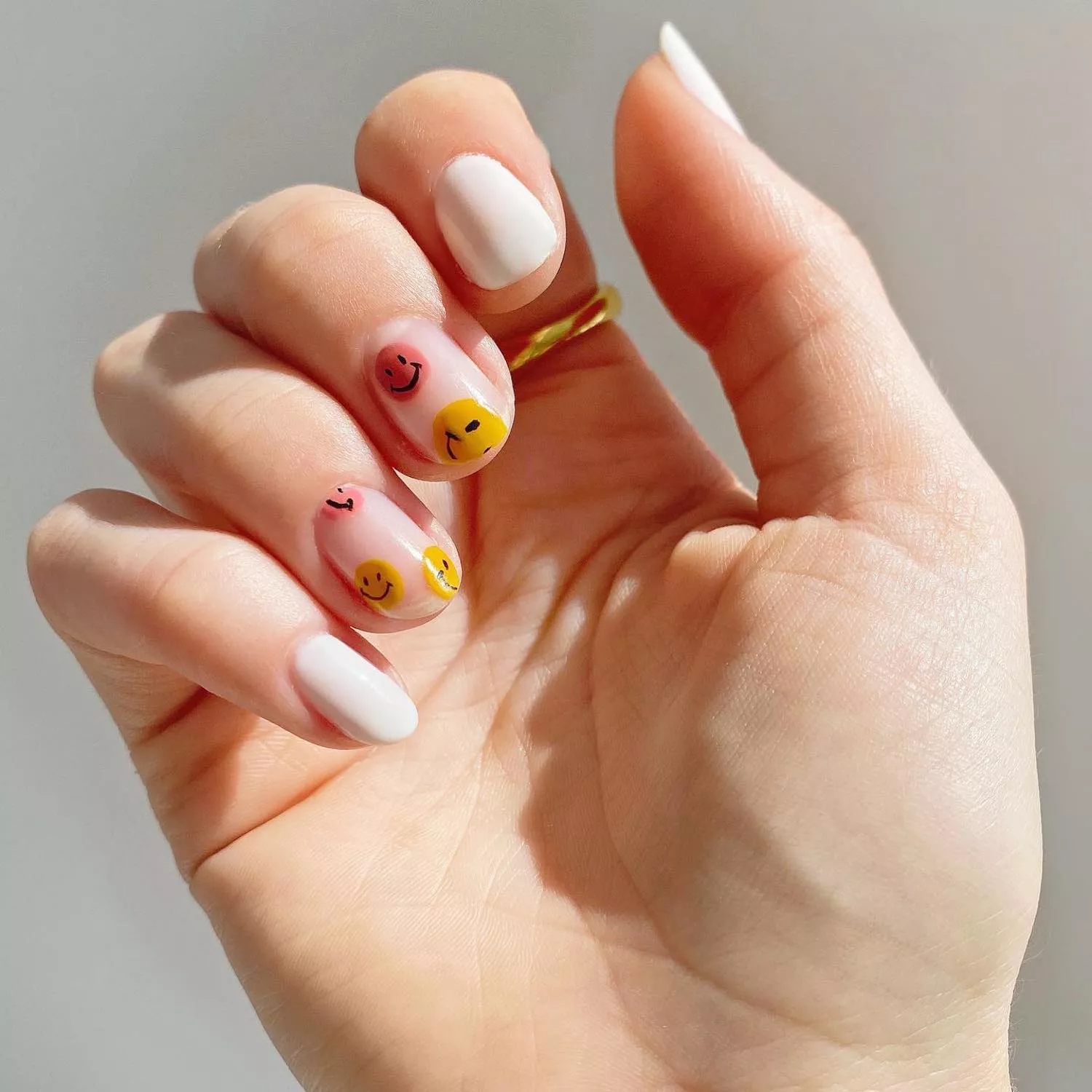 Manicure with white base and pink and yellow smiley face accent designs