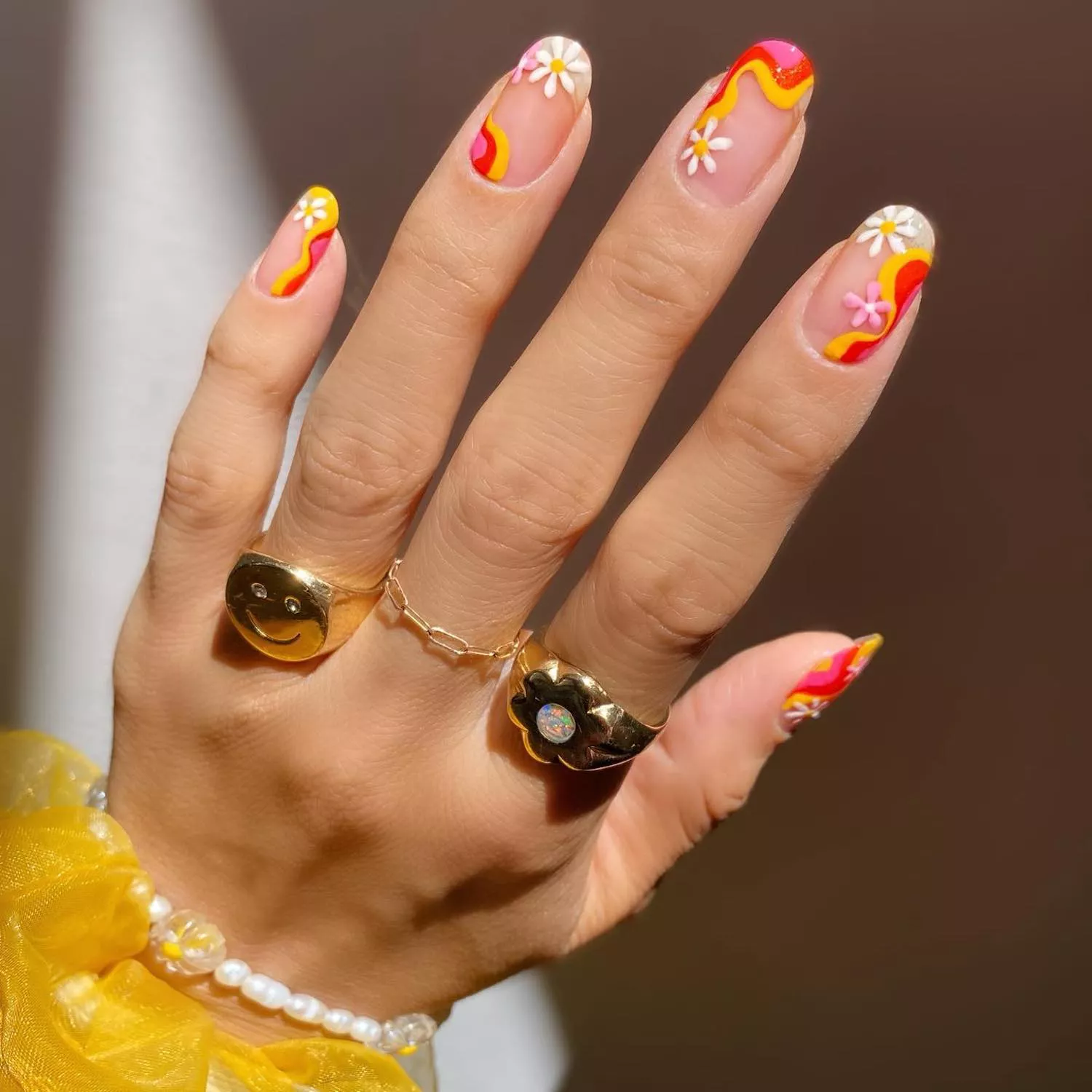 Manicure with pink, red, and yellow wavy design and pink and white daisies